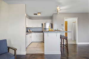 Kitchen with a breakfast bar, white cabinetry, light wood-style flooring, freestanding refrigerator, and a kitchen island