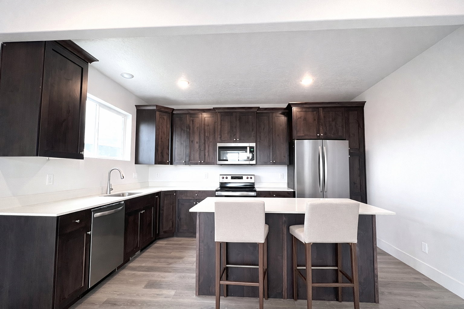 Kitchen with dark wood finish cabinets, stainless steel appliances, a kitchen island, light wood-type flooring, and recessed lighting
