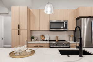 Kitchen featuring stainless steel appliances, modern cabinets, light wood finish cabinetry, and hanging light fixtures