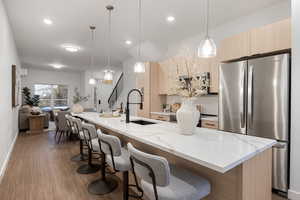 Kitchen featuring light wood finish cabinetry, freestanding refrigerator, decorative light fixtures, and light stone counters