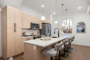 Kitchen featuring light wood finish cabinets, modern cabinets, hanging light fixtures, and a kitchen breakfast bar