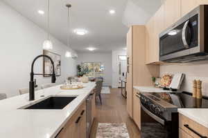 Kitchen with light wood finish cabinets, stainless steel appliances, modern cabinets, and decorative light fixtures
