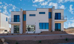 Rear view of house with a balcony, stucco siding, and stone siding