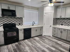Kitchen with gray cabinetry, black appliances, light wood-type flooring, and light stone countertops