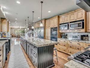 Kitchen featuring light stone countertops, a kitchen bar, stainless steel appliances, a large island, and hanging light fixtures