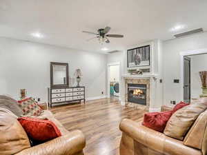 Living room with wood finished floors, a ceiling fan, a tile fireplace, and recessed lighting