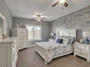 Bedroom featuring an accent wall, ceiling fan, and dark colored carpet