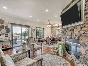 Living room featuring dark wood finished floors, healthy amount of natural light, ceiling fan, recessed lighting, and a stone fireplace