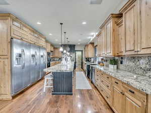 Kitchen featuring light stone countertops, a center island, light wood-type flooring, light wood finish cabinetry, and a breakfast bar