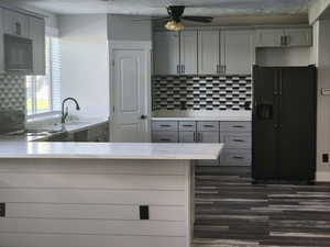 Kitchen with gray cabinetry, a peninsula, black appliances, and tasteful backsplash