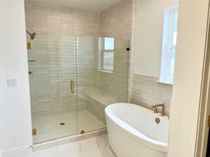 Full bathroom with a shower stall, a soaking tub, tile walls, and light marble finish flooring