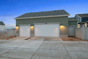 View of front of house with stucco siding, roof with shingles, driveway, an attached garage, and an outbuilding