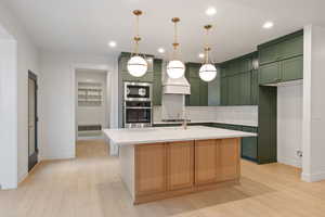 Kitchen featuring light stone countertops, light wood-type flooring, an island with sink, backsplash, and stainless steel appliances