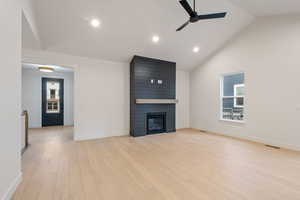Unfurnished living room featuring light wood finished floors, a fireplace, a ceiling fan, vaulted ceiling, and recessed lighting