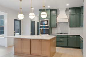 Kitchen featuring green cabinets, light wood-style floors, stainless steel appliances, tasteful backsplash, and a center island with sink