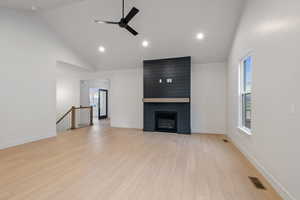 Unfurnished living room featuring light wood finished floors, a ceiling fan, vaulted ceiling, a large fireplace, and recessed lighting