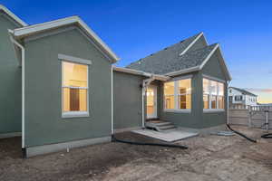 Back of house at dusk featuring a gate, stucco siding, and a shingled roof