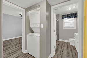 Laundry area with light wood finished floors, stacked washer / drying machine, and a textured ceiling