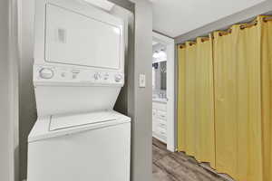 Laundry area with wood finished floors, stacked washer / dryer, and a textured ceiling