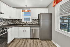 Kitchen featuring stainless steel appliances, dark countertops, white cabinetry, and pendant lighting