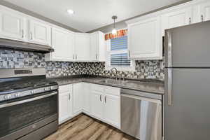 Kitchen with stainless steel appliances, dark countertops, white cabinets, and hanging light fixtures