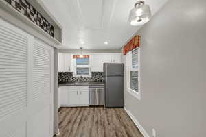 Kitchen featuring white cabinetry, stainless steel appliances, decorative light fixtures, and light wood-style floors