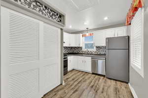 Kitchen with stainless steel appliances, white cabinets, hanging light fixtures, light wood-type flooring, and dark countertops