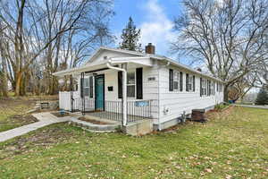 View of front of house featuring covered porch, a chimney, and a front yard