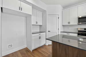 Kitchen with backsplash, white cabinets, stainless steel appliances, and dark wood-style floors