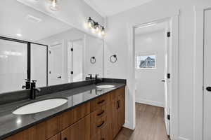 Full bath with double vanity and dark wood-style flooring