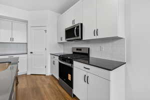 Kitchen featuring stainless steel appliances, white cabinetry, dark wood-style flooring, tasteful backsplash, and dark stone countertops