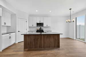Dual tone kitchen with dark wood-type flooring, an island with sink, suspended lighting, stainless steel appliances, and two tone cabinets