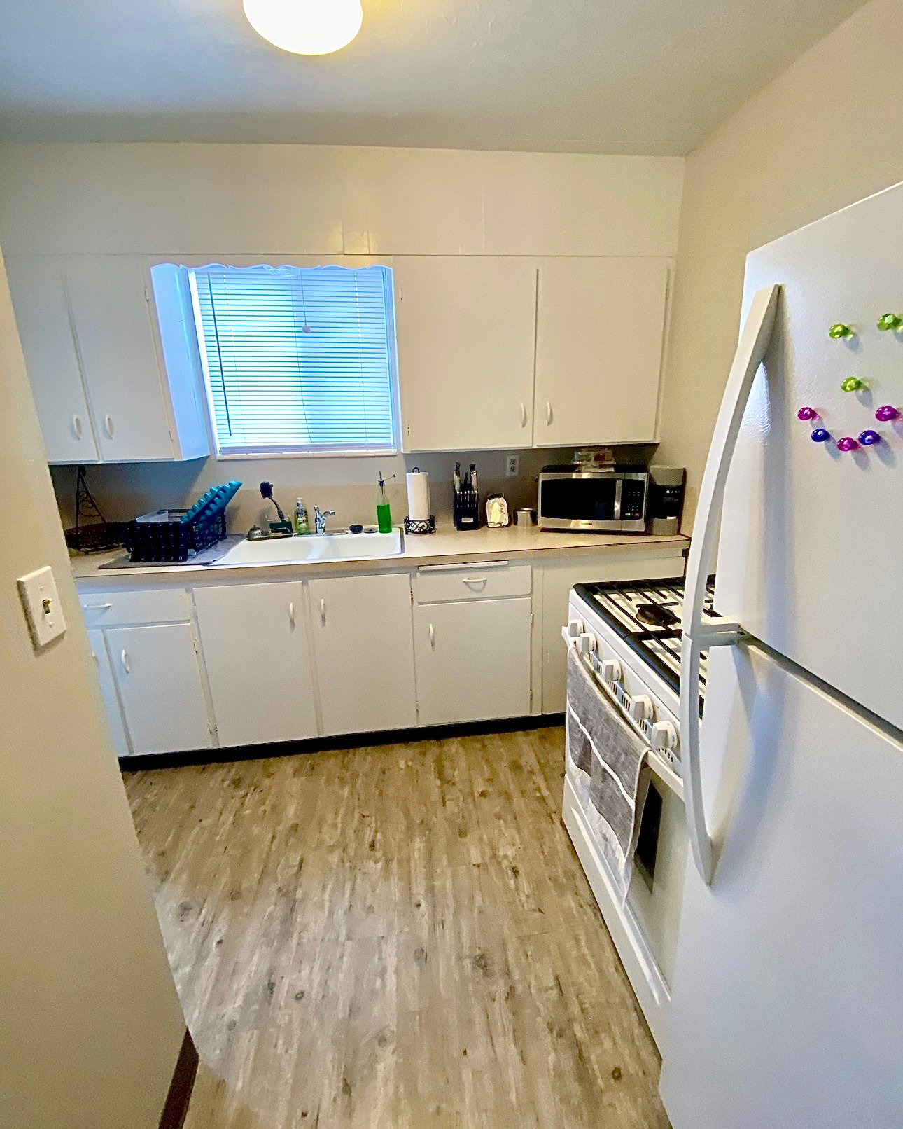 Kitchen with white appliances, white cabinetry, light countertops, and light wood-style flooring