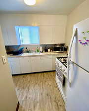 Kitchen with white appliances, white cabinetry, light countertops, and light wood-style flooring
