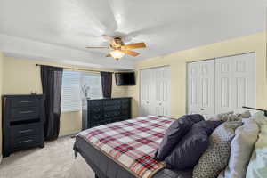Bedroom with multiple closets, light carpet, and ceiling fan