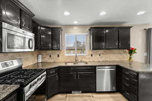 Kitchen featuring dark cabinets, stainless steel appliances, light stone counters, and recessed lighting