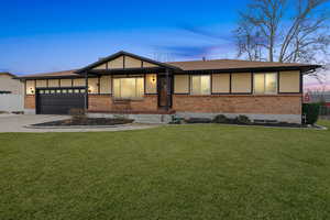 Ranch-style home with driveway, a garage, brick siding, and a yard
