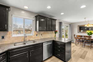 Kitchen with dark cabinetry, light stone counters, backsplash, dishwasher, and hanging lights