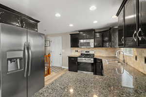 Kitchen featuring stainless steel appliances, dark stone counters, backsplash, dark cabinets, and light wood-type flooring