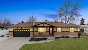 View of front of house featuring an attached garage, driveway, a shingled roof, and brick siding