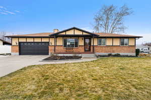 Single story home featuring brick siding, concrete driveway, an attached garage, and a front yard
