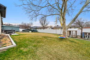Fenced backyard with exterior structure, an outbuilding, a residential view, a hot tub, and a mountain view