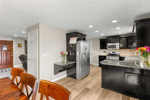 Kitchen with dark cabinets, light stone counters, stainless steel appliances, light wood-style floors, and recessed lighting