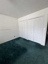 Unfurnished bedroom with dark carpet, two closets, and a textured ceiling