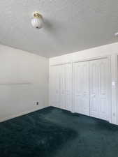 Unfurnished bedroom with dark carpet, multiple closets, and a textured ceiling