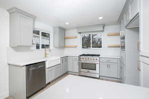 Kitchen with gray cabinets, open shelves, stainless steel appliances, recessed lighting, and light stone countertops