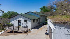 Exterior featuring a white brick facade, dark green shingles, a spacious wood-finish deck with black railings, and a detached structure with a green roof