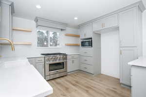 Kitchen with open shelves, stainless steel appliances, light wood-style flooring, recessed lighting, and gray cabinetry