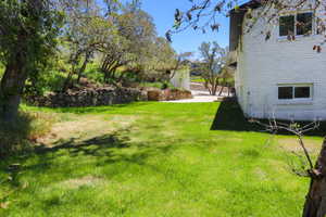 Expansive lawn area featuring mature trees, a stone retaining wall, and a white brick exterior