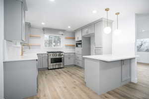 Kitchen with gray cabinetry, open shelves, decorative light fixtures, stainless steel appliances, and a peninsula